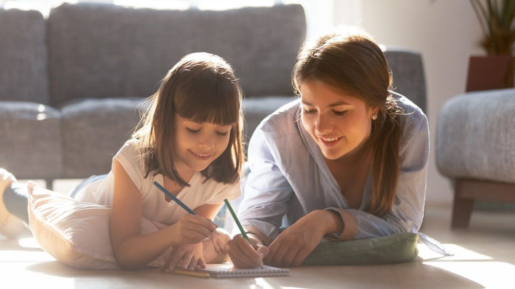 a mother and daughter lay together on the floor sketching and coloring